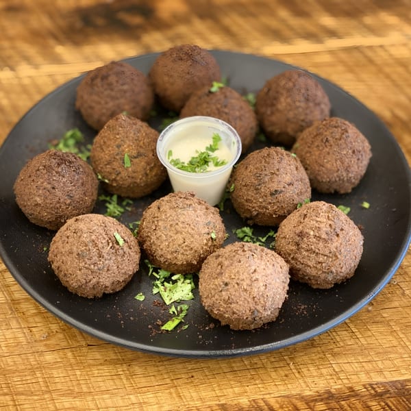 A black plate filled with round, brown falafel, garnished with parsley and a side of tahini sauce.
