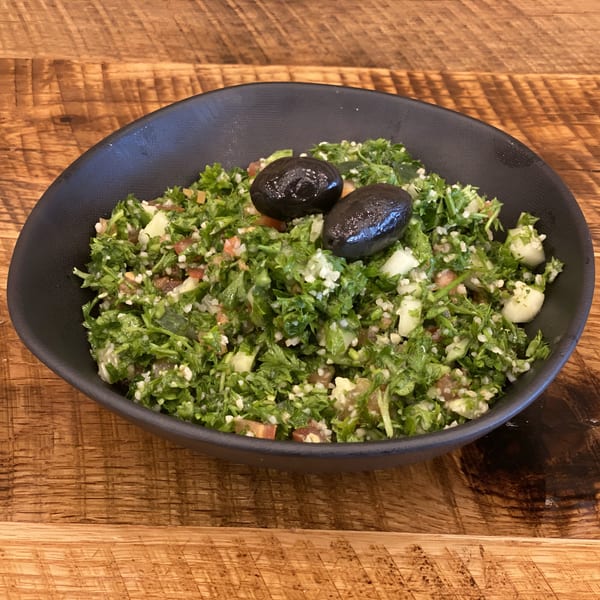 A black bowl of Jerusalem Bakery & Grill's tabbouleh salad with two black olives on a wooden table.