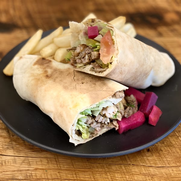 Two shawarma wraps with meat, lettuce, and pickles, served with french fries on a black plate.