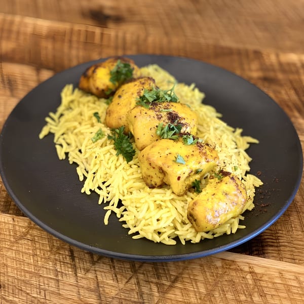 Middle-Eastern chicken and rice dish with parsley and spices on a black plate.