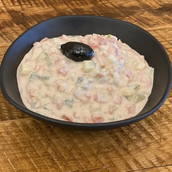 Creamy Jerusalem Bakery & Grill salad with diced vegetables and a black olive on a wooden table.