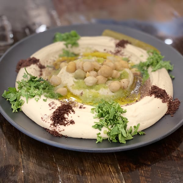 Creamy hummus topped with chickpeas, green sauce, olive oil, sumac, and fresh parsley.