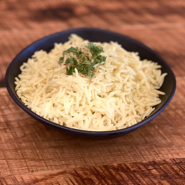 A black bowl filled with fluffy white rice, garnished with parsley and black pepper, on a wooden table.